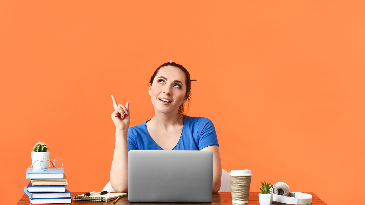 パソコンの前に座って人差し指を立てる女性の画像